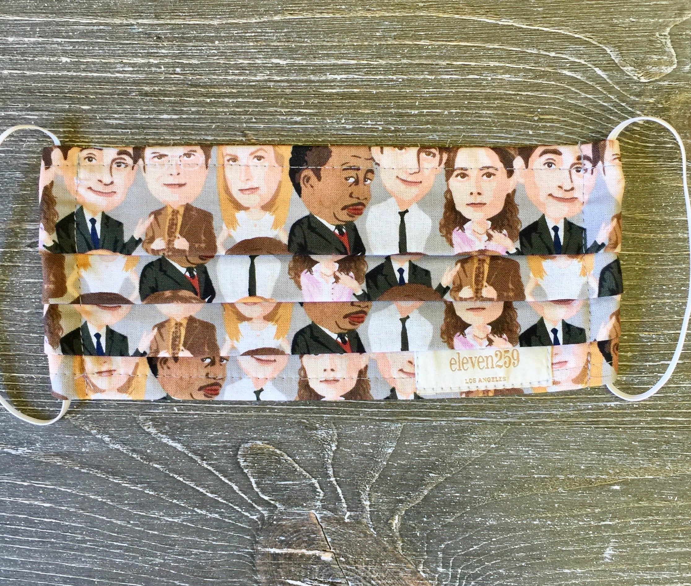 "the office" mask.  Mask features the faces of Pam, Dwight, Jim, Angela, and Stanley as characters on a cotton mask.  Mask has elastic and is 100% Cotton.  Hand washable 