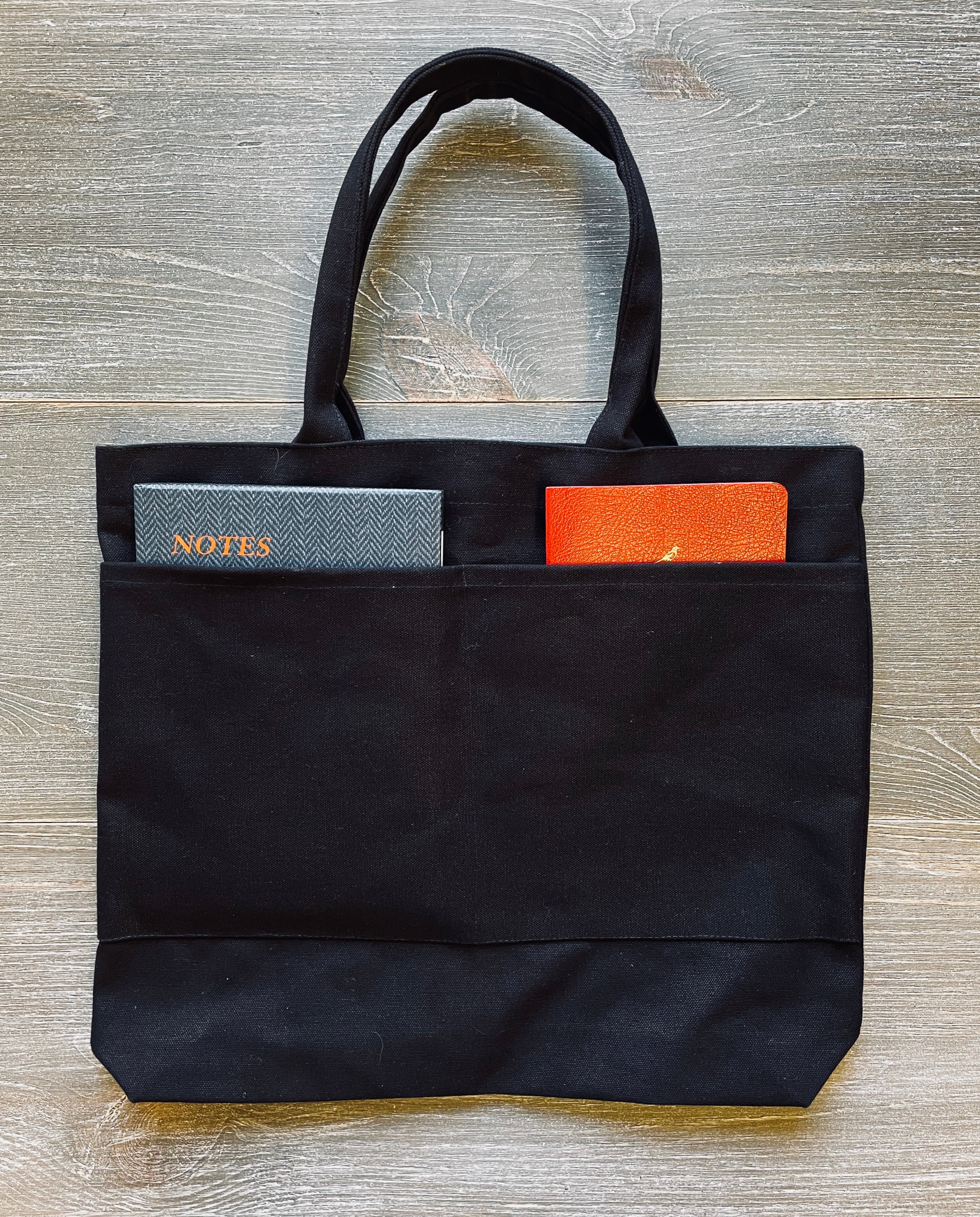 Black 12oz. Canvas Tote. One side has 2-9 inch outside pockets and the other side has eleven259 mission statement in lavender 